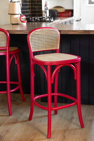 Two of the Chez Pitou Wood & Woven Cane Bar Stool in Red styled in a kitchen in front of a breakfast bar.