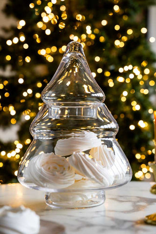 Clear glass Christmas tree-shaped container with meringues inside with a Christmas tree in the background.