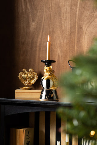The Circus Tiger Candlestick Holder with a lit candle inside, styled on a shelf with some other accessories with part of a Christmas tree also in shot.