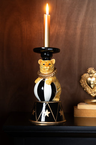 The Circus Tiger Candlestick Holder with a lit candle inside, styled on a shelf with some books and a tealight holder.