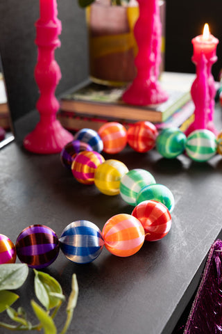 The Colourful Thread Bauble Christmas Garland styled on a dark surface with some hot pink candles.