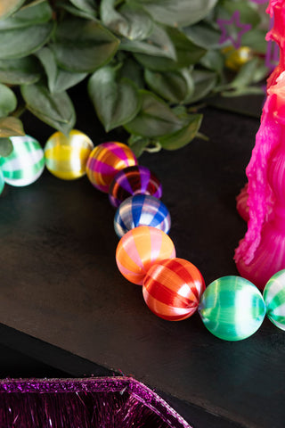 The Colourful Thread Bauble Christmas Garland on a dark surface with some greenery, candles and a tinsel garland.