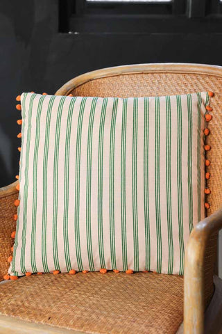 Lifestyle image of the Cotton Green Stripe Cushion with Orange Pom-Poms
