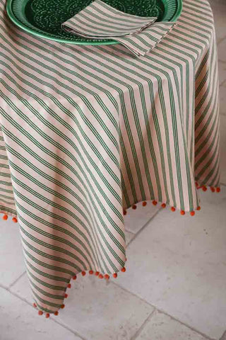 Lifestyle image of the Cotton Green Stripe Table Cloth with Orange Pom-Poms