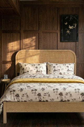 The Curved Wood & Rattan Bed styled with printed bedding, in front of a wooden panelled wall with a framed art print on.