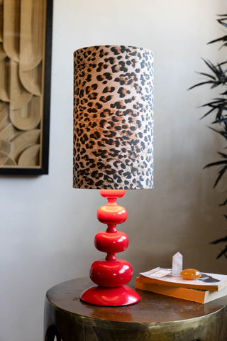 Curve Red Table Lamp With Leopard Shade shown with the light on and styled sat on a gold side table against neutral wall. 