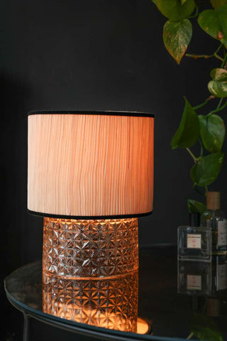 Lifestyle image of the Amber Parisian Table Lamp on displayed on a tabletop with bottles of fragrance and a plant. 