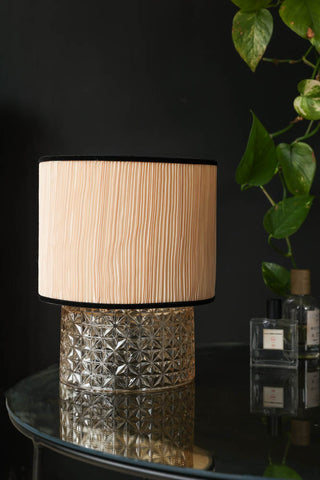 Lifestyle image of the Amber Parisian Table Lamp displayed on a tabletop with bottles of fragrance and a plant. 