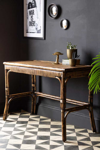 The Dark Brown Rattan Console styled with various home accessories, on a geometric floor next to a black wall.