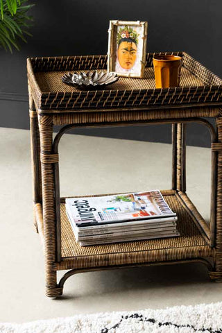 Lifestyle image of the Dark Brown Rattan Side Table styled with various home accessories and magazines.