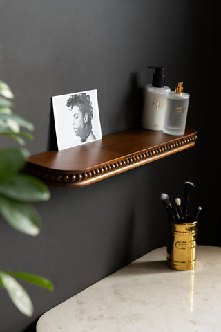 The Dark Wood Bobbin Floating Shelf  shown against a black wall with beauty products and a post card on the shelf. 