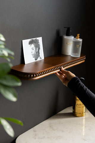 The Dark Wood Bobbin Floating Shelf shown with beauty products and a hand in shot for scale. 