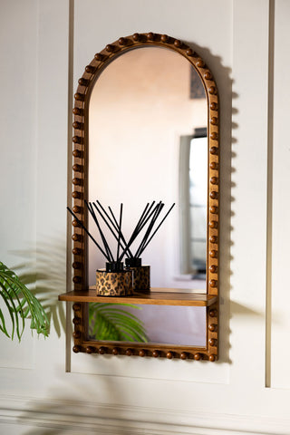 The Dark Wood Bobbin Mirror With Shelf shown on a panelled wall with a diffuser on the shelf. 