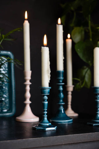 The Deep Blue Enamel Cast Style Candlestick Holders and Pink Enamel Cast Style Candlestick Holders displayed together with lit candles inside, styled with a matching blue tray and a plant.