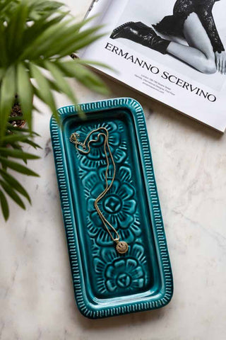 The Deep Blue Enamel Cast Style Trinket Tray displayed on a marble table with a necklace inside, styled with a plant and a book.