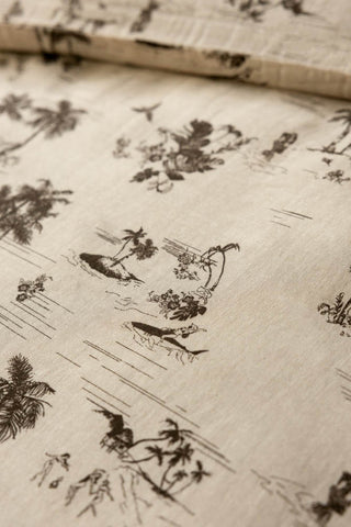 Close up of the print of the Desert Island Cotton Muslin Bedding Set, showing palm trees and a woman on a bikini riding a shark