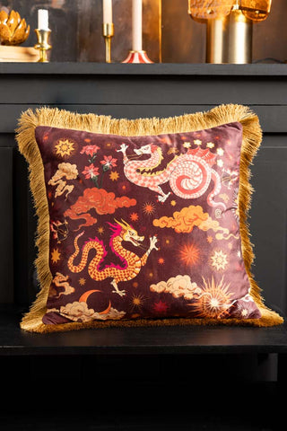 The Dreamland Dragon Fringed Velvet Cushion styled on a black bench.