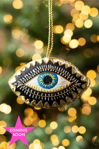 The Embroidered Blue Eye Hanging Christmas Tree Decoration hanging in front of fairy lights. Image shown with a pink star that reads 'coming soon'.