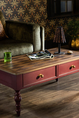 The Emporium Brick Red Coffee Table shown in a living room setting with a green velvet armchair and palm wallpaper on the walls. 