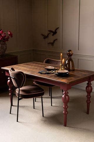 The Emporium Brick Red Extendable Dining Table shown with chocolate brown dining chairs and leopard print plates against neutral panelled walls. 