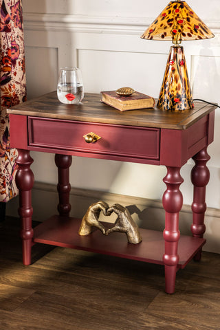 The Emporium Brick Red Side Table shown against neutral panelled walls with gold and lips accessories including a water glass and table lamp. 