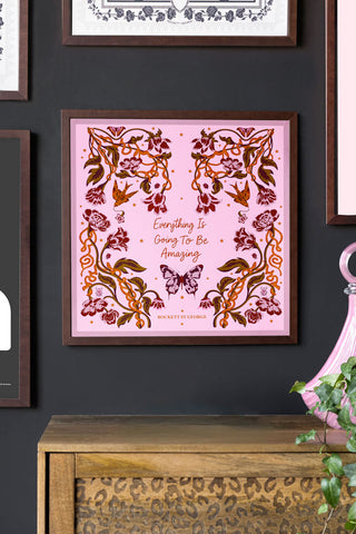 Framed pink artwork with floral designs and text on a dark wall with wooden furniture.