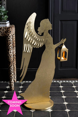 The Extra Large Gold Angel Decorative Lantern with a lit candle inside, displayed on a geometric floor with a leopard print table in the background. The image has a pink star with the words "coming soon" displayed across the star. 