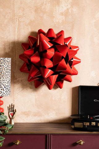 The Large Red Gift Bow Christmas Decoration styled on the wall above a sideboard with various accessories on.
