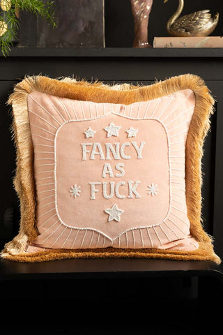 The Fancy As Fuck Double-Fringed Pink Velvet Cushion styled on a black bench with some accessories in the background.