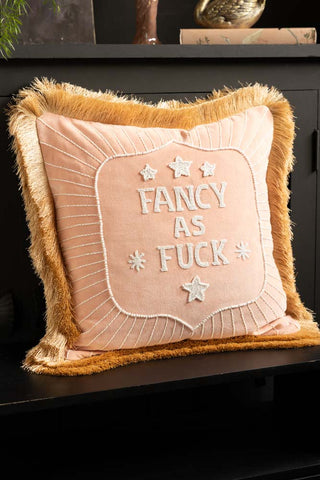 The Fancy As Fuck Double-Fringed Pink Velvet Cushion styled on a black bench in front of a cabinet with some accessories on.