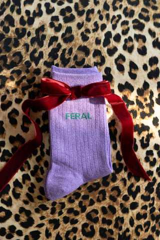 The Feral Cotton Glitter Socks shown against a leopard print background with a red ribbon on top of the socks. 