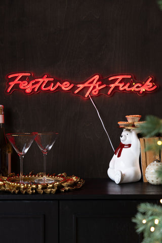 Neon sign reading 'Festive As Fuck' on a dark background with decorative items.