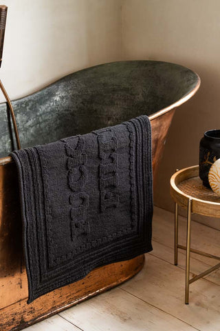 Black bath mat draped over the edge of a metal bath.