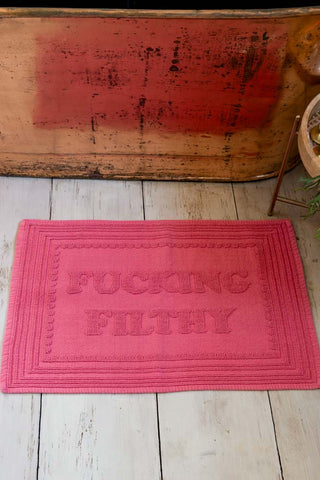Image shows the Fucking Filthy Hot Pink Bath Mat styled in front of a copper bath. 