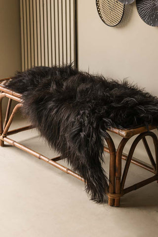 Lifestyle image of the Genuine Icelandic Long Wool Sheepskin - Natural Black, styled on a wicker bench in the corner of a neutral room.
