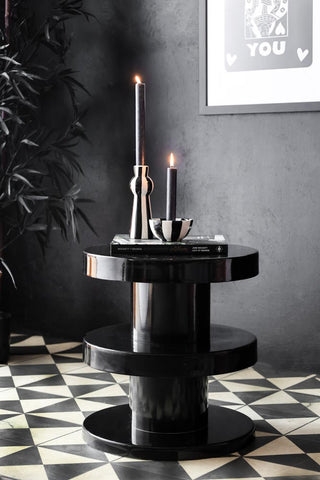 Black glossy side table in a dark moody setting styled with monochrome candlesticks.