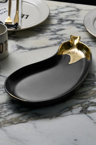 The Gold Aubergine Serving Bowl displayed on a marble worktop, with plates, a mug, napkin and cutlery in the background.