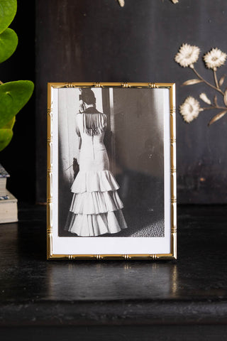 Lifestyle image of the Gold Bamboo Effect Photo Frame on a shelf with dark styling and a plant