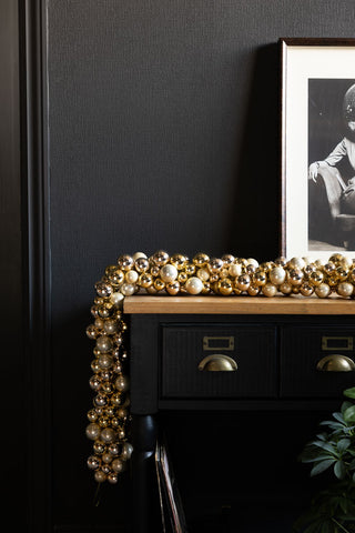 The Gold Bauble Cluster Christmas Garland draped on a console table with an art print and some greenery.