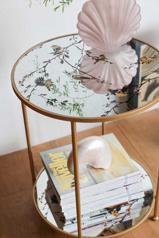 Lifestyle image of the Gold Beautiful Birds Mirror Side Table styled with decorative accessories. 