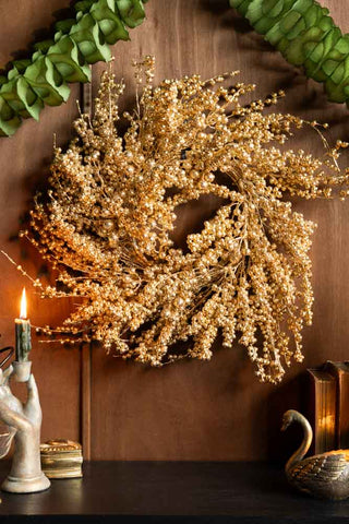 The Gold Berry Christmas Wreath styled on a wall surrounded by accessories.