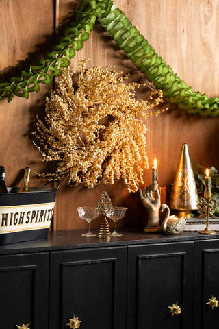The Gold Berry Christmas Wreath on a wall above a sideboard styled with various accessories.