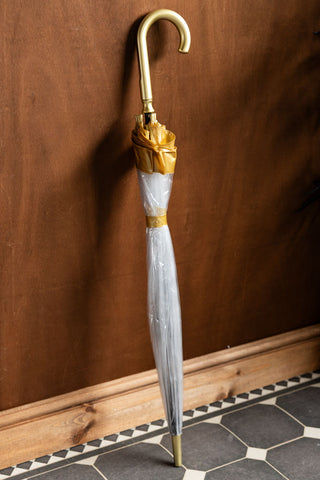 The Clear & Gold Domed Umbrella shown closed and leaning against a wood wall. 