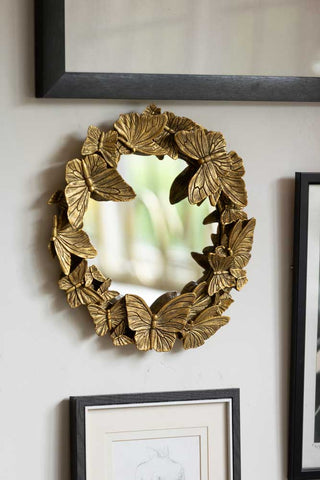 Lifestyle image of the Gold Butterfly Mirror on a white wall surrounded by art prints in frames. 