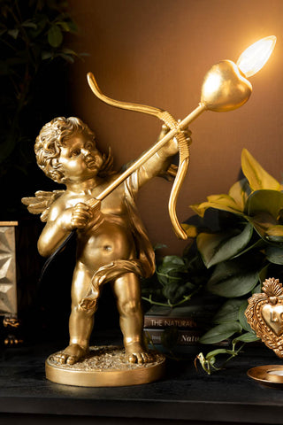 The Gold Cupid Table Lamp styled on a lack sideboard with some accessories and greenery.
