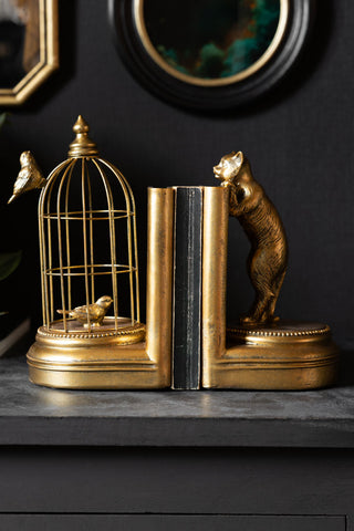 The Gold Curious Cat Bookends styled with a book, on a dark wooden surface.