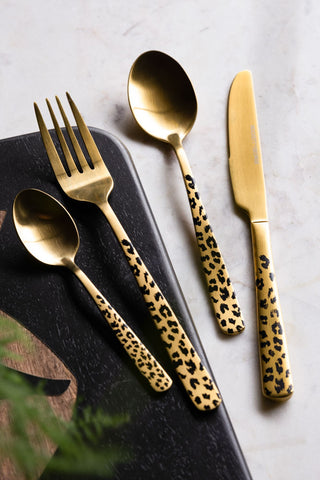 The Gold Leopard 16 Piece Cutlery Set, showing gold cutlery with a black leopard print pattern against a marble surface and black chopping board. 