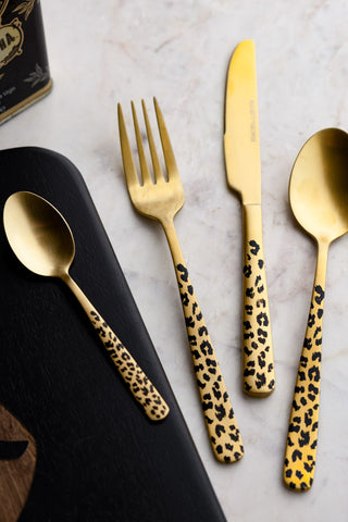 The Gold Leopard 16 Piece Cutlery Set, showing the teaspoon, fork, knife and spoon against a marble surface and black chopping board. 