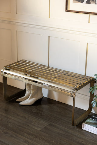 Gold Metal Bench shown in a hallway against panelled walls with a pair of cowboy boots styled underneath. 