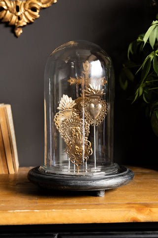 The Gold Milagro Hearts Glass Dome shown with the glass cloche against a black wall. 